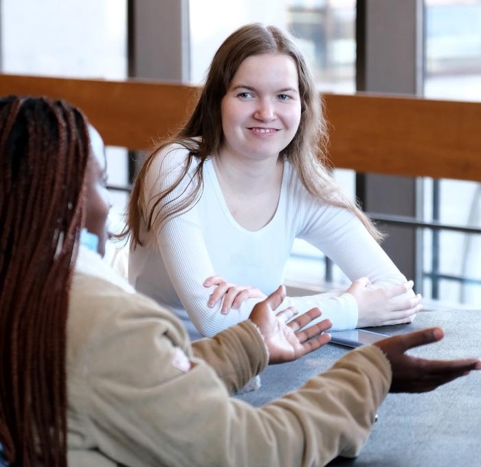 Smiling female students in the main lounge sitting at a table. 